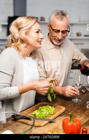 homme souriant qui verse du vin et femme tenant du basilic vert Banque D'Images