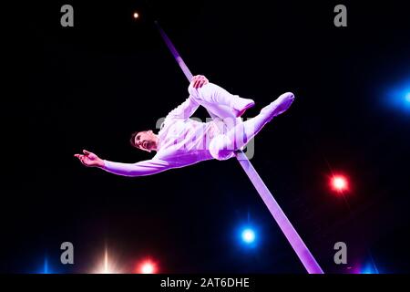 rétro-éclairage près du beau acrobat tenant le poteau métallique pendant la performance dans le cirque Banque D'Images