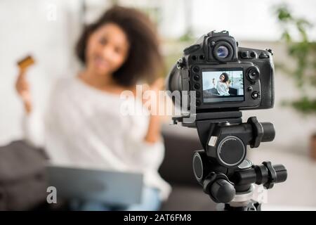 mise au point sélective de l'appareil photo numérique avec une fille africaine américaine en bretelles tenant la carte de crédit et montrant le pouce vers le haut sur l'affichage Banque D'Images