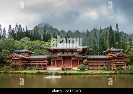 Kaneohe, Oahu, Hawaï, États-Unis. - 11 janvier 2020 : murs bordeaux et toit gris, temple bouddhiste de Byodo-In avec étang de koi en face, arbres verts et montagne Banque D'Images