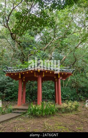 Kaneohe, Oahu, Hawaï, États-Unis. - 11 janvier 2020 : petit pavillon de médiation avec piliers bordeaux dans le jardin du temple bouddhiste de Byodo-In. Feuilles de verdure bac Banque D'Images