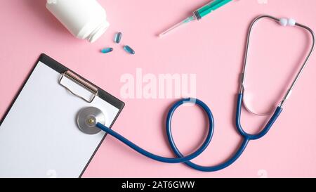 Concept de contrôle médical. Matériel médical sur fond rose. Vue du dessus table des médecins avec stéthoscope, presse-papiers médicaux, seringue, pilules. Santé Banque D'Images