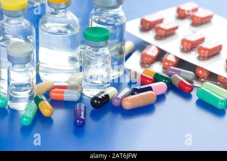 De nombreuses capsules de médicaments de couleur différente et un paquet de feuilles avec divers flacons de vaccins par injection sur un plateau bleu Banque D'Images