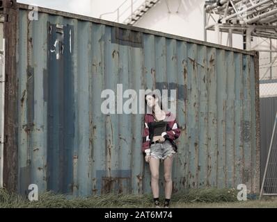 Jeune fille moderne debout par vieux bien utilisé grungy regardant le conteneur de fret désaturé pour l'effet vieux fané. Banque D'Images