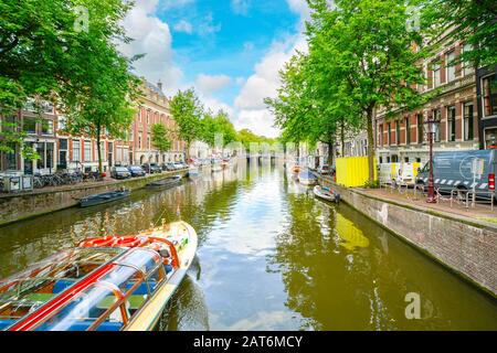 Un bateau de tourisme voyages un pittoresque canal d'Amsterdam sur un après-midi à la fin de l'été Banque D'Images