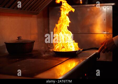 Flambe. Feu dans la poêle à frire. Chef professionnel dans une cuisine commerciale. Faites frire des aliments dans une poêle moulante sur la table de cuisson dans la cuisine extérieure Banque D'Images