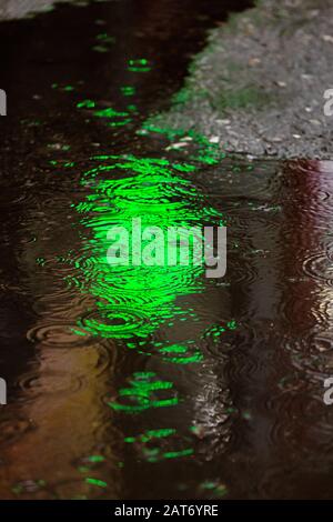 Jour de pluie. Une flaque avec des gouttes de pluie et des réflexions d'une pharmacie de lanterne verte dans une flaque. Paysage urbain, photographie de rue Banque D'Images