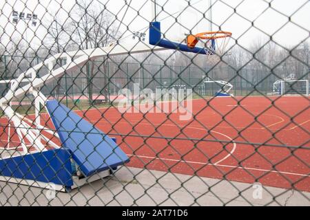 Un stand de basket-ball portable et réglable se ferme dans une cour de sport extérieure, vide derrière la clôture métallique Banque D'Images