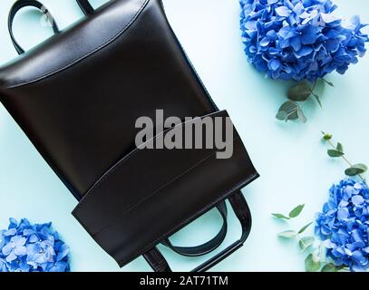 Sac à dos en cuir noir avec fleurs hortensia bleu sur un fond bleu clair. Banque D'Images