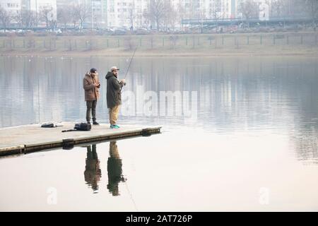 Belgrade, Serbie - 26 janvier 2020: Les gens se tenant sur un quai de fer pendant la pêche Dans le lac Ada en hiver, et leur réflexion sur l'eau Banque D'Images