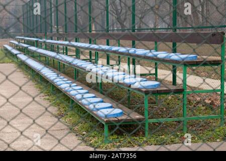 Les gradins du Grand stand sont dotés de sièges en plastique bleu dans un petit stade, derrière la clôture métallique Banque D'Images