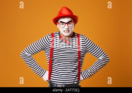 Jeune mime avec des gants blancs et un chapeau rouge sur fond orange vide Banque D'Images