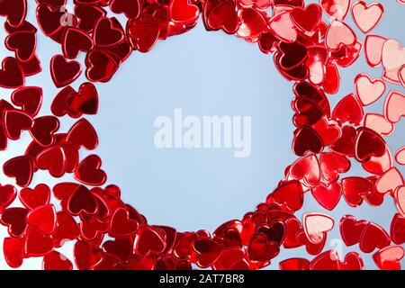 Confettis en forme de coeur disposés en un cadre circulaire sur fond bleu. Banque D'Images