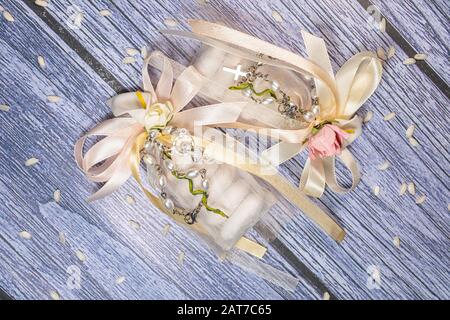 Faveurs de mariage. Boîtes avec ruban rose et or contenant des confettis et un petit cadeau de rosaire chrétien. Banque D'Images