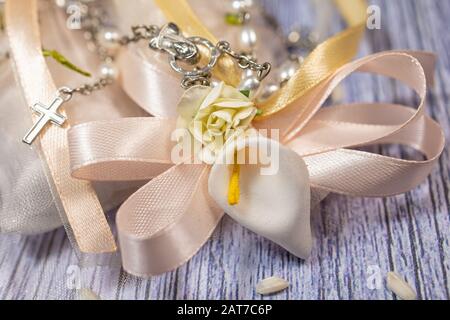 Faveurs de mariage. Boîtes avec ruban rose et or contenant des confettis et un petit cadeau de rosaire chrétien. Banque D'Images