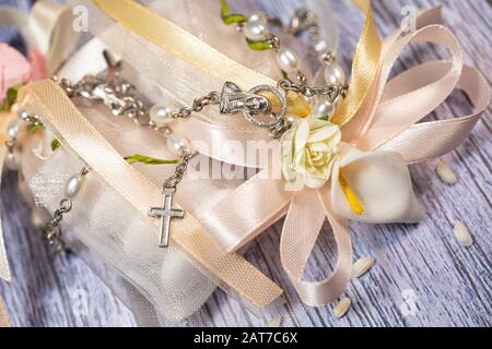 Faveurs de mariage. Boîtes avec ruban rose et or contenant des confettis et un petit cadeau de rosaire chrétien. Banque D'Images