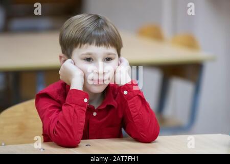 Enfant étudiant en école primaire. Un garçon dans une chemise rouge à la table. Banque D'Images