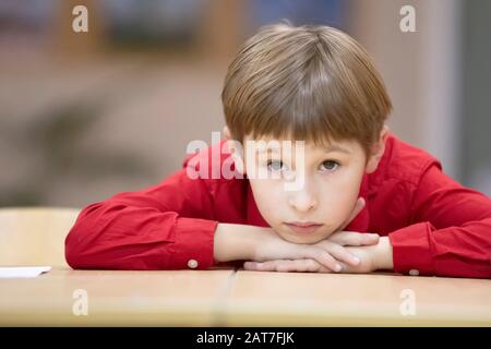 Enfant étudiant en école primaire. Un garçon dans une chemise rouge à la table. Banque D'Images