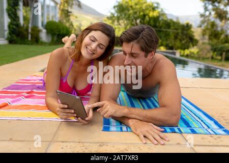 Un jeune couple heureux utilisant une tablette près de la piscine Banque D'Images