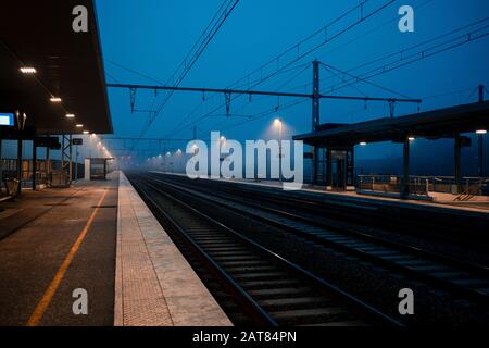Une épaisse brume s'installe sur une gare européenne vide et des voies ferrées en France au crépuscule pendant l'heure bleue. Banque D'Images