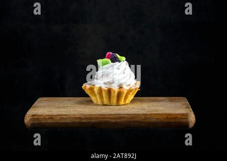 Gâteau à la crème blanche décoré de baies sur un panneau en bois sur fond noir.Beau dessert sucré. Banque D'Images