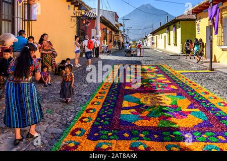 Antigua, Guatemala - 14 avril 2019 : la famille Maya et le tapis de procession du dimanche de Palm avec le volcan Agua derrière sur le site du patrimoine mondial de l'UNESCO. Banque D'Images