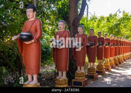 Rangée de statues de moine bouddhiste avec des peignoirs rouges et des bols d'almes dans les jardins du temple bouddhiste à Siem Reap Banque D'Images