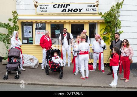 Famille portant des rubans rouges à l'extérieur de la boutique de Fish and chips Chip Ahoy pendant les célébrations d'Obby Oss, Padstow, Cornwall, Royaume-Uni Banque D'Images