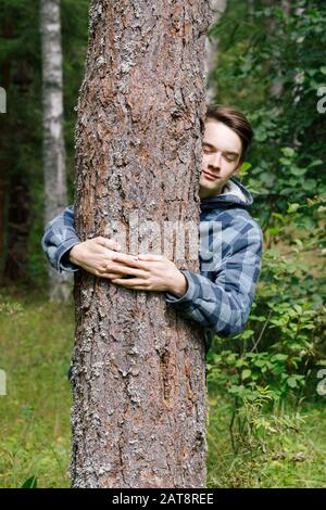 Adolescent garçon embrassant le pin dans une forêt d'été penchant au tronc d'arbre avec des yeux fermés embrassant la nature Banque D'Images