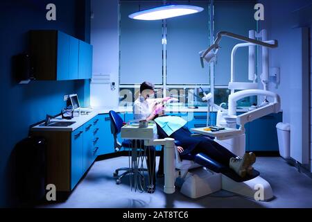 Femme dentiste très soigneusement vérifier et réparer la dent de son jeune patient féminin. Heureuse jeune femme assise dans une chaise dentaire au bureau de dentiste Banque D'Images