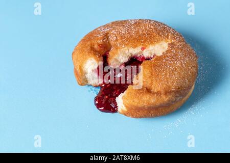 Beignet allemand avec remplissage de confiture de framboises sur fond bleu sans couture. Image macro d'un anneau avec bourrage. Dessert maison. Bonbons célèbres. Banque D'Images