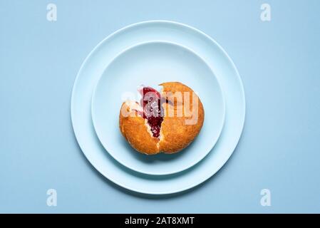 Un seul beignet de berliner tranché, avec de la confiture de framboises sur des plaques bleues et un arrière-plan sans couture. Vue sur l'anneau de gelée fait maison. Célèbre donut allemand Banque D'Images