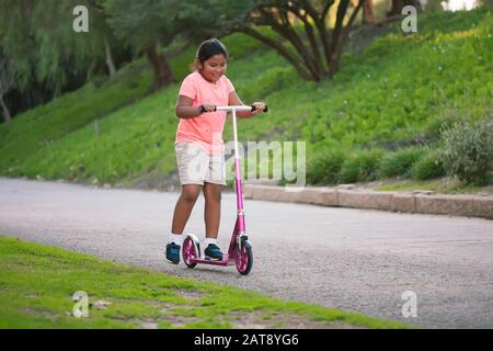 Une jeune fille qui monte un scooter rose dans une rue étroite. Banque D'Images