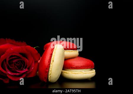 Macarons . macarons rouges sur fond noir avec rose rouge pour la Saint Valentin Banque D'Images