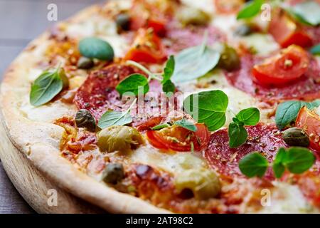 Pizza avec salami, olives vertes, fromage mozzarella, câpres et basilic frais. Fond en bois marron Banque D'Images