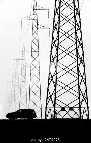 Voiture près des lignes pour la transmission générale de l'électricité dans un paysage brumeux Banque D'Images