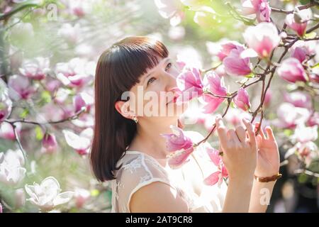 la femme possède une branche de magnolia avec des fleurs roses. Allergie à la floraison au printemps. Risque de gonflement du quintessentiel. Banque D'Images