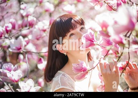 la femme possède une branche de magnolia avec des fleurs roses. Allergie à la floraison au printemps. Risque de gonflement du quintessentiel. Banque D'Images