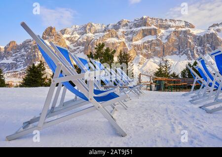 Des rangées de chaises longues pour bronzer sur la neige dans les Dolomites, en Italie, avec le groupe Sella comme toile de fond au coucher du soleil. Banque D'Images