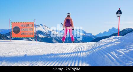 Skieur féminin sur le bord d'une piste de ski noire, en regardant la distance, à côté d'un panneau de pente disant Difficile pente en italien, allemand, et anglais, je Banque D'Images