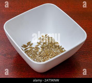 Macro photo de graines de cumin dans un bol blanc sur une table en bois Banque D'Images