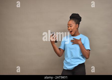 belle jeune fille africaine utilisant son téléphone mobile se sentant heureuse et surprise Banque D'Images