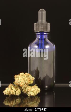 CBD huile en bouteille de verre bleu avec compte-gouttes et fleurs de marijuana sur surface noire réfléchissante Banque D'Images