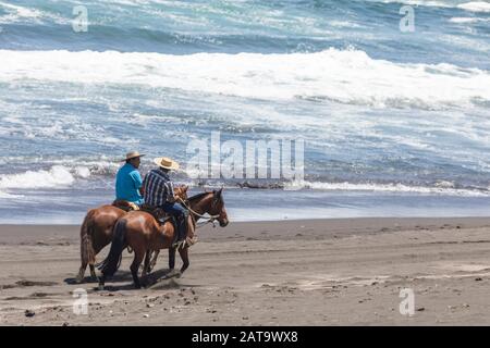 Deux hommes sur une promenade à cheval autour de la côte chilienne Dans une plage de sable au crépuscule heure d'été à la plage appréciant la nature chilienne et ses plages sauvages Banque D'Images