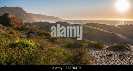 Magnifique coucher de soleil sur la vue sur l'eau de la côte chilienne. Un paysage de plage idyllique avec la lumière du soleil illuminant les dunes de sable avec des couleurs orange Banque D'Images