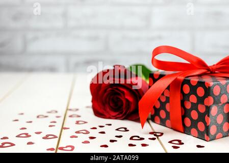 Rose rouge, boîte cadeau et petits coeurs sur table en bois blanc avec espace de copie pour le texte. Concept de carte de Saint-Valentin et de carte de fête des mères. Banque D'Images