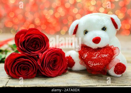 Concept de Saint Valentin. Ours en peluche blanc et roses rouges sur une vieille table en bois devant un fond lumineux flou. Mise au point sélective. Banque D'Images