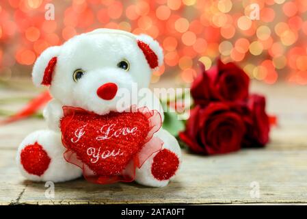 Concept de Saint Valentin. Ours en peluche blanc et roses rouges sur une vieille table en bois devant un fond lumineux flou avec espace de copie pour le texte. Banque D'Images