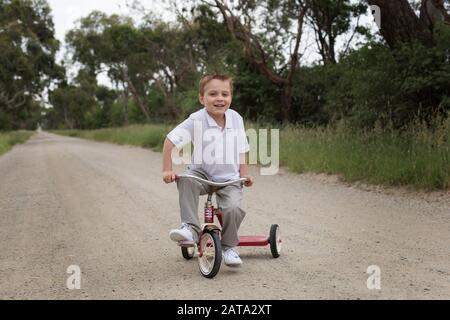 Un garçon australien caucasien qui fait du tricycle sur une route de terre dans le pays Banque D'Images