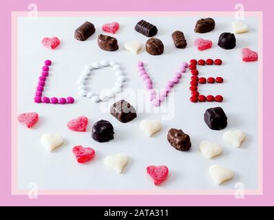 Les friandises sont disposées sous la forme d'un mot amour, entouré de bonbons. Isolé sur blanc avec une bordure rose Banque D'Images